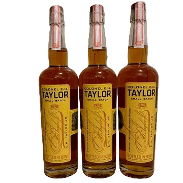 Three bottles of Colonel E.H. Taylor small batch whiskey on a wooden surface.